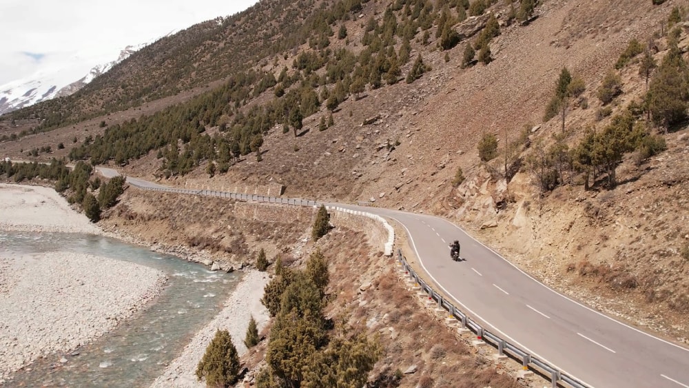 Motorcyclist riding on a guarded mountain road alongside a river in the Himalayas